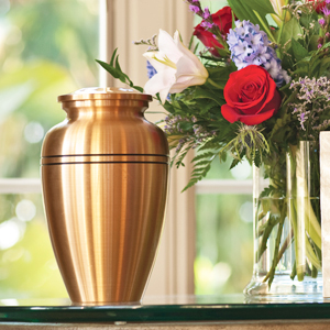 Bronze colored urn sitting on a table next to a bouquet of flowers